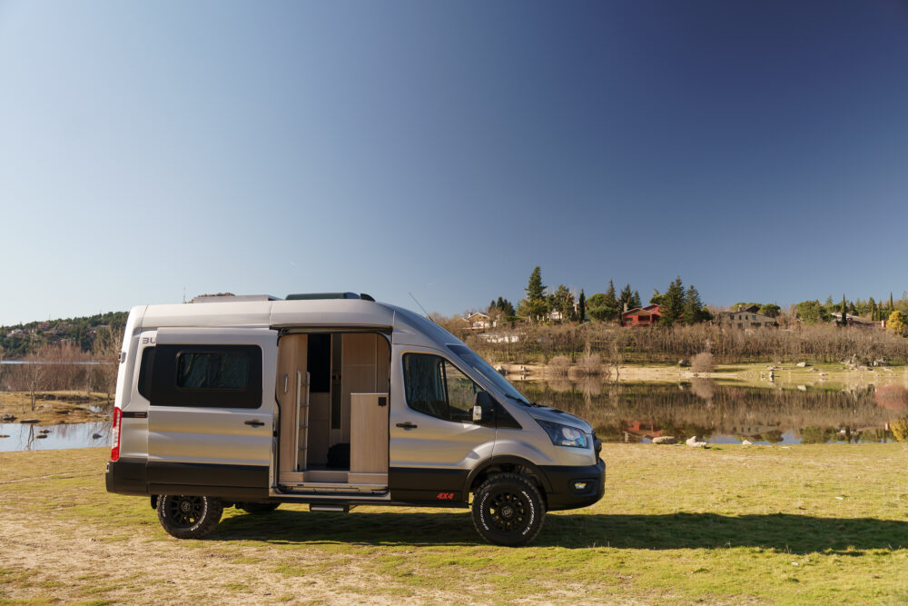 vista lateral de ford transit 4x4 camperizada en prado verde con lago al fondo